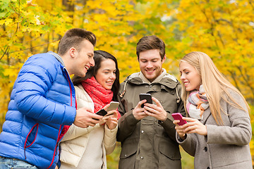 Image showing smiling friends with smartphones in city park