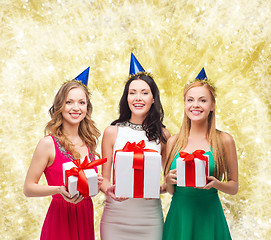 Image showing smiling women in party caps with gift boxes