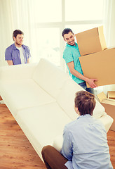 Image showing smiling friends with sofa and boxes at new home