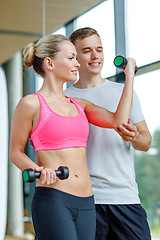 Image showing smiling young woman with personal trainer in gym