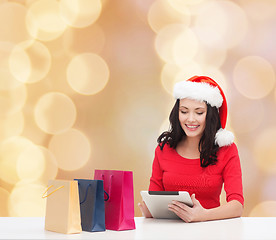 Image showing smiling woman in santa hat with bags and tablet pc