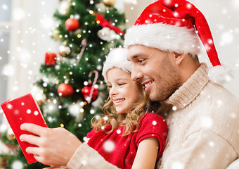 Image showing smiling father and girl in santa hats reading book