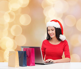 Image showing smiling woman in santa hat with bags and laptop