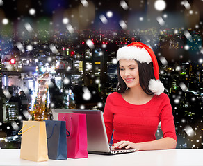 Image showing smiling woman in santa hat with bags and laptop