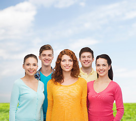 Image showing group of smiling teenagers over blue sky and grass