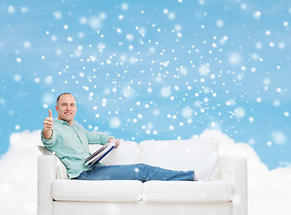 Image showing smiling man with book showing thumbs up on sofa