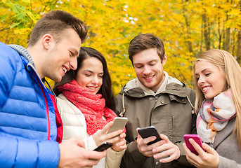 Image showing smiling friends with smartphones in city park