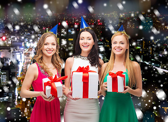 Image showing smiling women in party caps with gift boxes