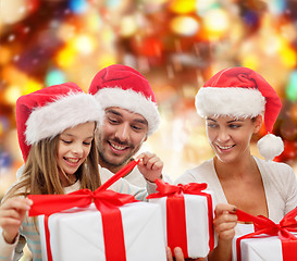 Image showing happy family in santa hats sitting with gift boxes