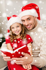 Image showing smiling father and girl in santa hats reading book