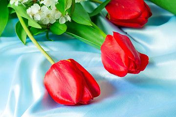 Image showing Three bright red tulips against blue silk