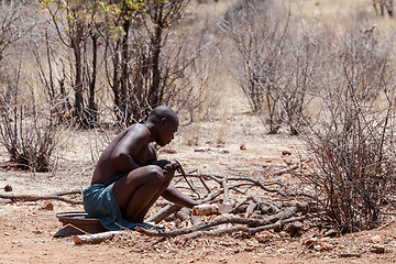Image showing Himba man adjusts wooden souvenirs in fireplace for tourists