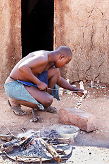 Image showing Himba man adjusts wooden souvenirs in fireplace for tourists