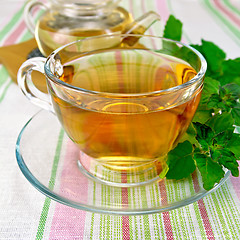 Image showing Tea with mint in cup and teapot on tablecloth
