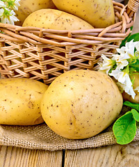 Image showing Potatoes yellow with flower and basket on wooden board