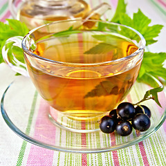 Image showing Tea with blackcurrants in cup on tablecloth