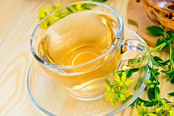 Image showing Tea from tutsan in glass cup on board with flowers