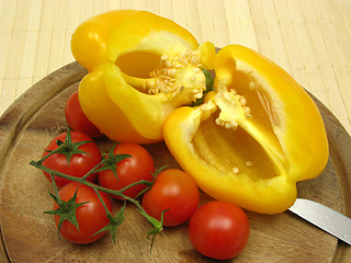 Image showing Halved yellow pepper and tomatoes on wooden plate  with knife