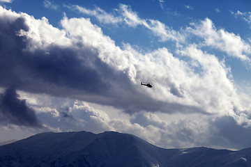 Image showing Helicopter in cloudy sky and winter mountains