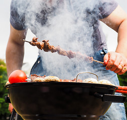 Image showing Chef covered in smoke grilling skewers of meat and vegetables ov