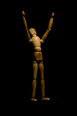 Image showing Wooden mannequin raising hands to light isolated on black.