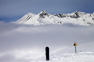 Image showing Warning sing, snowboard on off-piste and mountains in fog