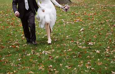 Image showing Bride and groom running on grass