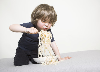 Image showing Child eating spaghetti on the sofa