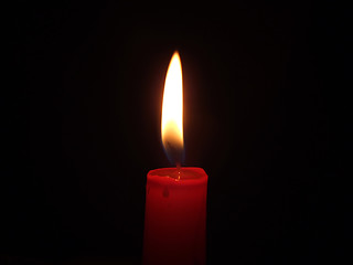 Image showing The red candle burning in full darkness