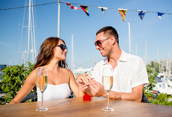 Image showing smiling couple with champagne and gift at cafe