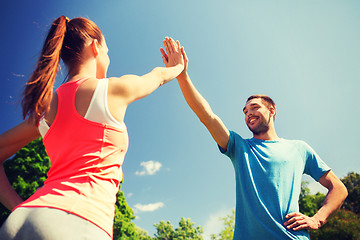 Image showing two smiling people making high five outdoors