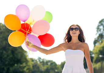 Image showing smiling young woman in sunglasses with balloons