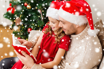 Image showing smiling father and girl in santa hats reading book