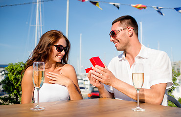 Image showing smiling couple with champagne and gift at cafe