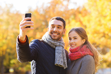 Image showing smiling couple with smartphone in autumn park
