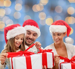 Image showing happy family in santa hats sitting with gift boxes