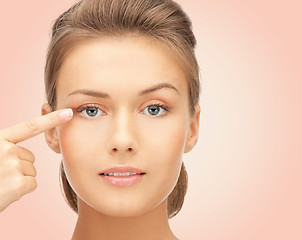 Image showing beautiful young woman pointing finger to her eye