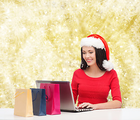 Image showing smiling woman in santa hat with bags and laptop