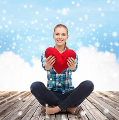 Image showing young woman with red heart pillow sitting on floor