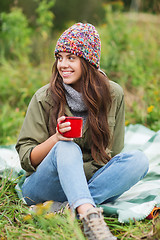 Image showing smiling young woman with cup sitting in camping