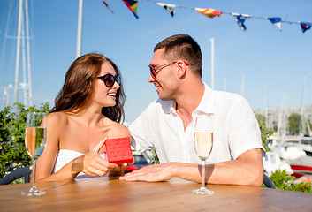 Image showing smiling couple with champagne and gift at cafe