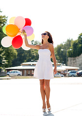 Image showing smiling young woman in sunglasses with balloons