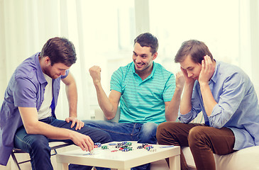 Image showing happy three male friends playing poker at home