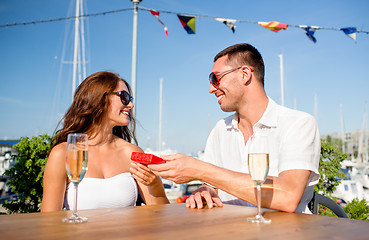 Image showing smiling couple with champagne and gift at cafe