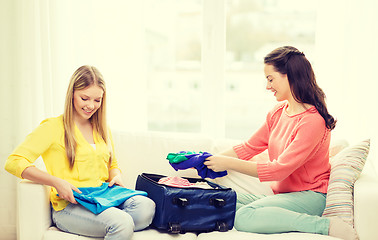 Image showing two smiling teenage girls packing suitcase at home