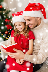 Image showing smiling father and girl in santa hats reading book