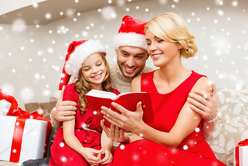 Image showing smiling family in santa hats reading book at home