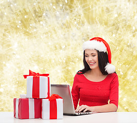 Image showing smiling woman in santa hat with gifts and laptop