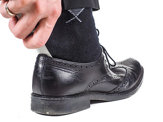 Image showing Male hand entering foot with black sock into black leather shoe 