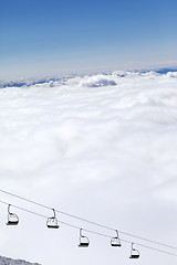 Image showing Chair-lift and mountains under clouds in sun day